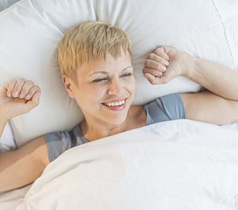 Smiling woman in bed stretching after sleep apnea treatment in Waverly